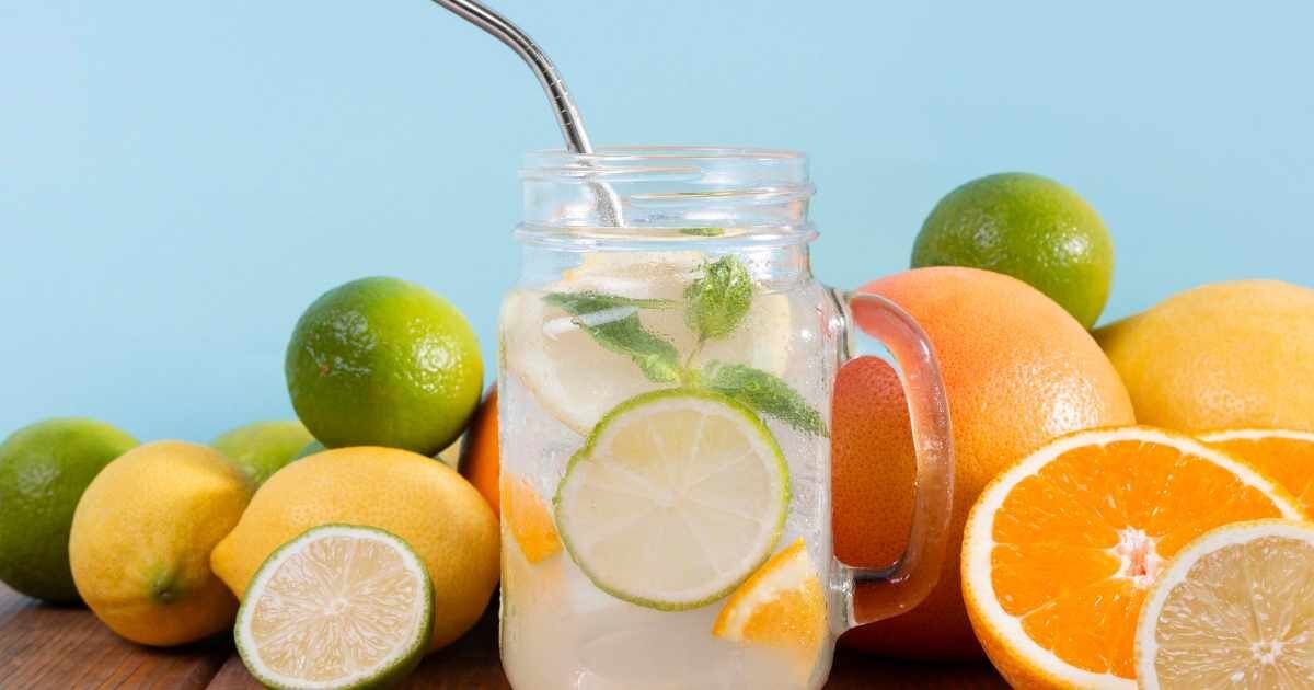 Mason jar of fresh citrus-infused water surrounded by limes, lemons, and oranges.